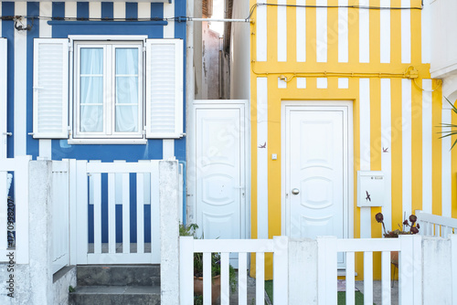 Colorful blue and yellow striped house facades with white doors and fences in a narrow street, showcasing vibrant coastal architecture and charming urban contrast