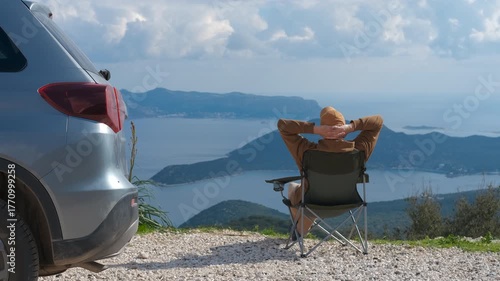 Tourist relaxing and folding chair near car enjoying sea bay view. Serene road trip moment featuring young traveler relaxing on folding chair, taking in panoramic sea bay scenery before packing up
