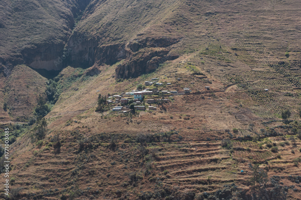 Obraz premium A small, remote village nestled on a steep, arid mountainside in the Andes of Peru. Agricultural terraces are visible on the slopes, showing traditional rural life in South America.