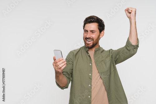 Head shot overjoyed happy millennial Caucasian man holding smartphone, looking at screen, reading lottery winner notification, celebrating achievement, isolated on white studio background.