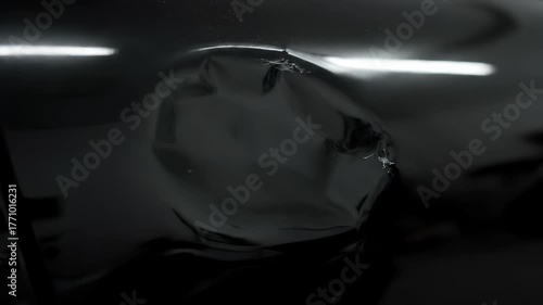 Close-up of a distorted, reflective, and dark surface, possibly a wrapped object or a damaged material.