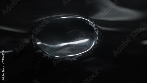 Close-up shot of a reflective, dark, and glossy liquid droplet with a blurred background.