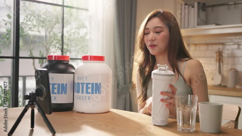 Young Asian female health influencer live streaming on social media sharing nutrition tips with whey protein powder by smartphone. Healthy lifestyle, fitness coaching, clean eating. online marketing.