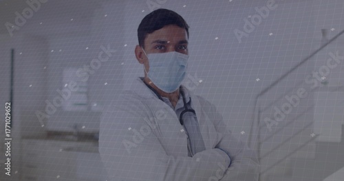 Standing adult physician wearing lab coat and mask in hospital corridor, with stethoscope