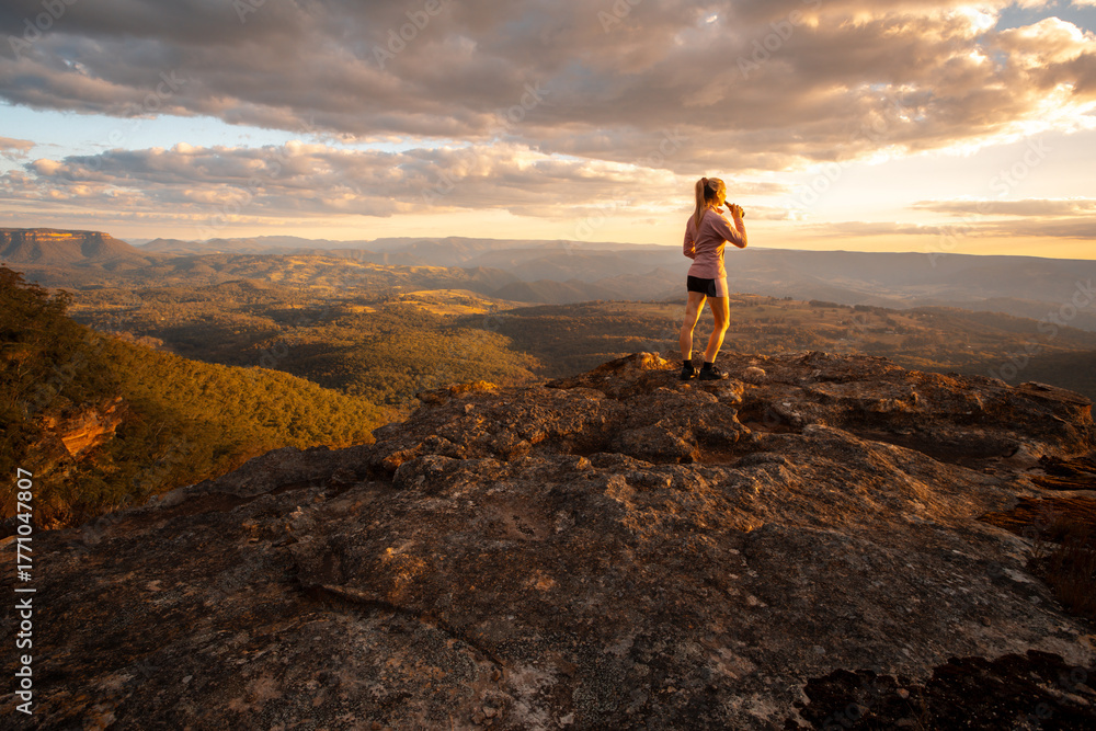 Fototapeta premium Woman on rock with drink looking at mountain valley views