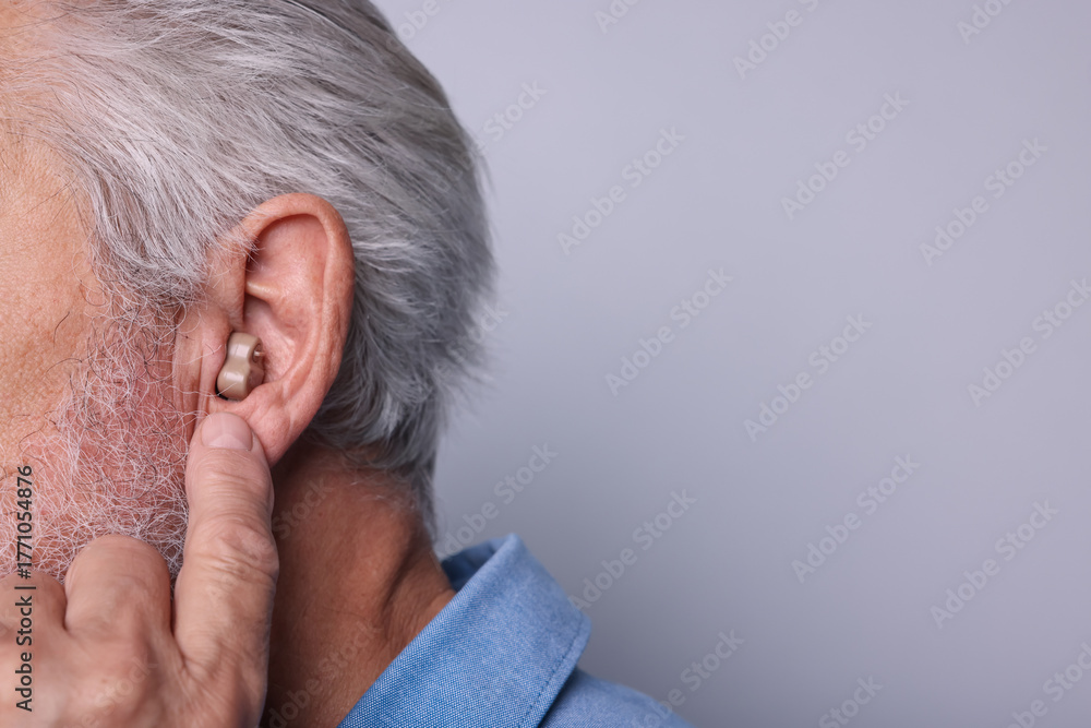 Fototapeta premium Senior man with hearing aid on light grey background, closeup