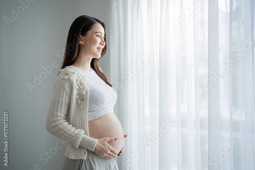 Asian young pregnant woman gently holds and strokes her belly in house. Free Download Asian young pregnant woman gently holds and strokes her belly in house. - GFXLoad
