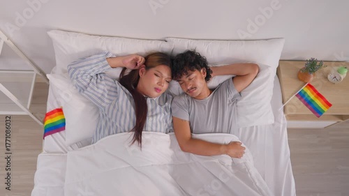 Asian transgender woman and male partner lying down, sleeping on bed. 