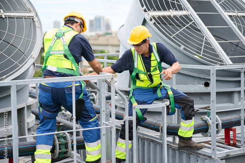 Construction workers collaborating on a rooftop, emphasizing safety and teamwork in an industrial setting. They are wearing safety helmets and harnesses