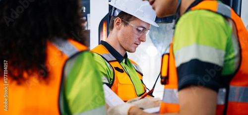 Industrial workers wearing safety gear are discussing project plans and reviewing technical documents on the modern factory manufacturing. Teamwork collaboration on construction site