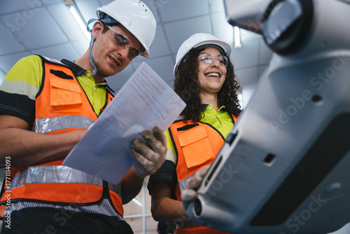 Experienced engineer in safety gear collaborating to operate and inspect a high-tech CNC machine and check technical documents on the production factory. Teamwork at automation industry