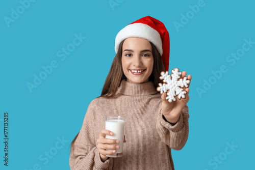Young woman with tasty Christmas gingerbread cookie and milk on blue background