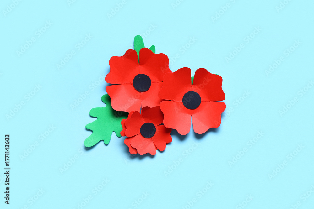 Obraz premium Paper poppy flowers and leaves on blue background. Remembrance Day