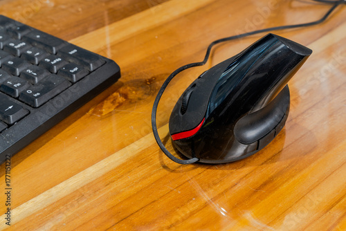 Vertical ergonomic computer mouse with red accent and wired connection on wooden desk next to black keyboard, showcasing comfortable tech setup for workspace efficiency