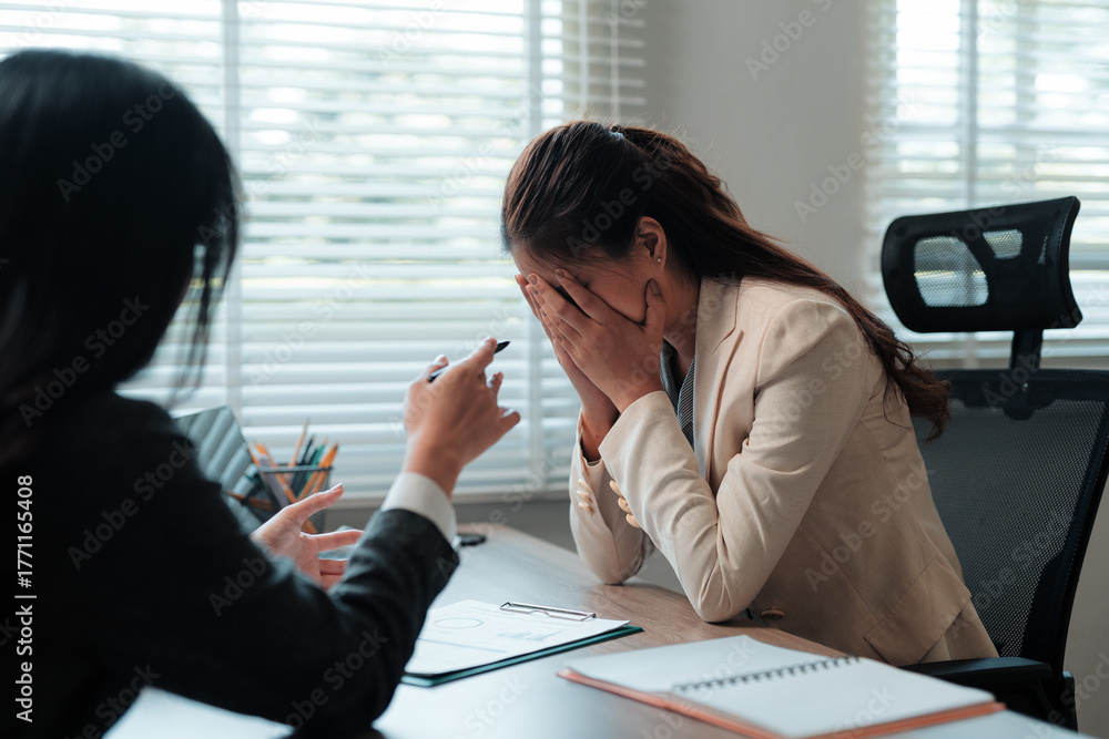 © Crystal - Young businesswoman experiencing stress and burnout, covering her face in frustration during a difficult conversation with a colleague
