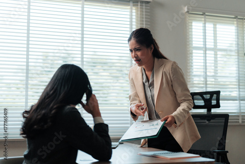 Angry female boss confronting a stressed employee, holding a document and discussing business problems in an office setting