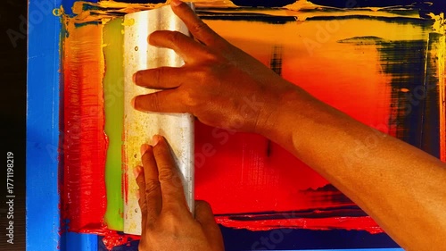 Colorful screen printing workshop scene where red, orange, and yellow inks merge across the mesh screen, illustrating the intricate manual process of creating bold and dynamic gradient prints by hand