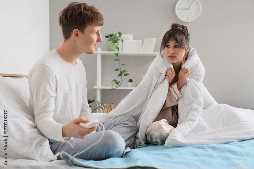 Obraz premium Young couple turning on electric heating pad in bedroom