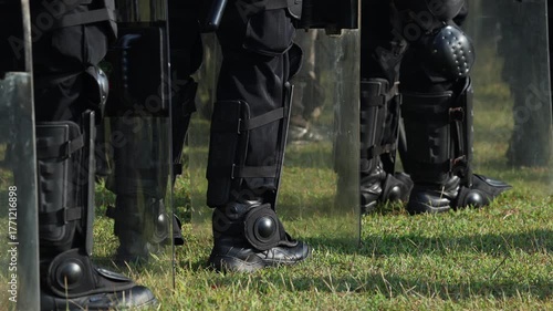 Legs of Anti-riot squad. Heavily armored special police forces create barricade on the street. Close up of boots. Tactical armed policeman on protest. Riot police team in black uniform. Demonstration
