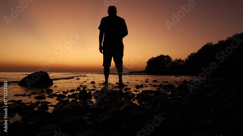 4k man standing on the beach on golden hour sunset. Enjoying the spectacle of the sun. Sunset Landscape. 
