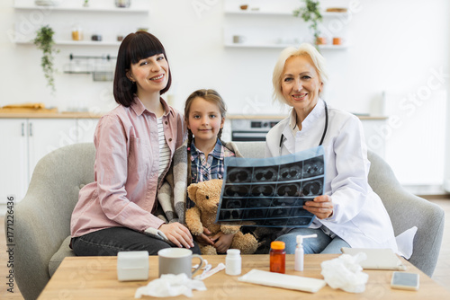A doctor reviews an X-ray with a mother and daughter. The scene takes place in a home setting, with medical supplies on the table.