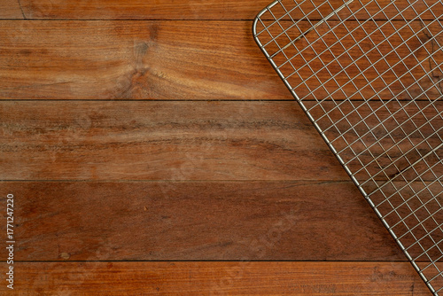 A top-down, flat-lay view of a metal wire cooling rack, designed to promote air convection, resting in the corner of a dark, natural wood plank tabletop.