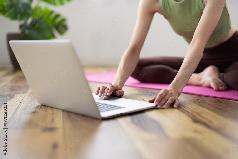 Naklejka premium Laptop-Focused Shot of Middle-Aged Asian Woman Taking Online Yoga Class at Home