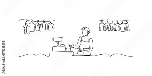 Shop worker at counter with clothing on racks behind