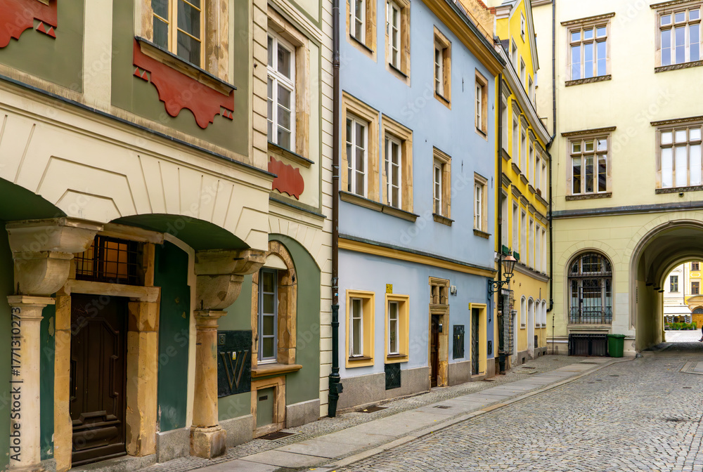 Obraz premium Colorful townhouses along narrow cobbled street in Wroclaw Old Town, restored facades, historic urban architecture, archway passage, quiet pedestrian area without traffic
