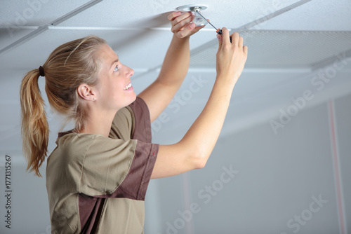 Canvas Print female construction worker or electrician replacing light bulb