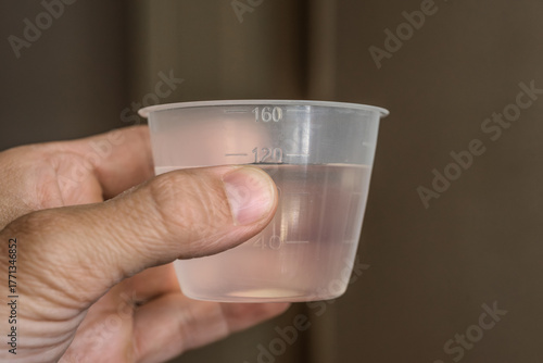 Closeup photo of male hands holding plastic measuring cup with liquid. Hand holding a transparent measuring cup with water for home or medical use.