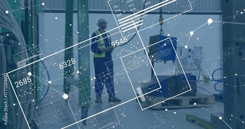 Factory tech in helmet and vest examining component hanging from crane hook, with data overlays