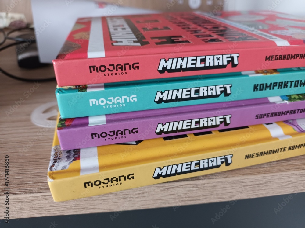 Naklejka premium A stack of colorful official Minecraft handbooks by Mojang Studios in the Finnish language, resting on a wooden shelf