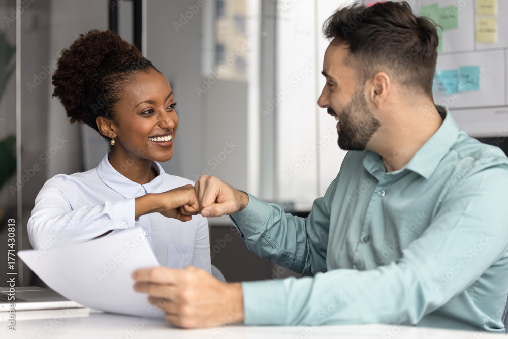 Fototapeta premium Excited multiracial diverse project partners reviewing papers share fist bump