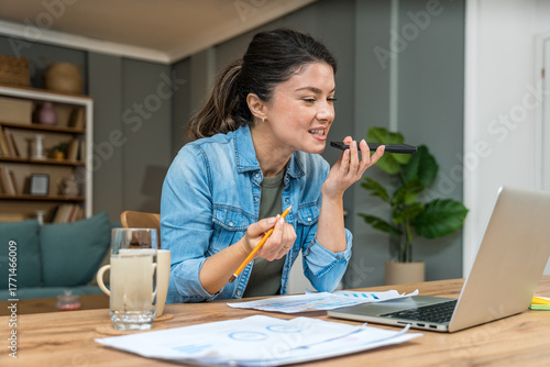Valokuva Freelance businesswoman in home office reviewing charts and dictating a voice no