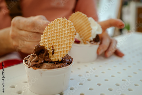 The photo of woman enjoys creamy Italian gelato on a sunny day in Italy. She stands outdoors near a street café, holding ice cream with waffle decor. Summer atmosphere, daylight, travel, Italian city
