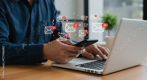 Office worker managing multiple email alerts on phone and laptop, illustrating business communication, technology, and information overload
