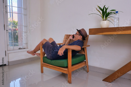 Bild auf Leinwand man casually lying on the armchair, making a phone call