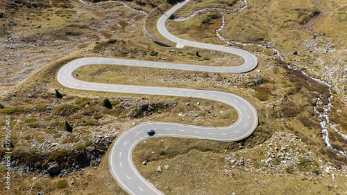 Aerial view of a winding road cutting through the rugged, autumnal landscape, with a solitary car navigating its curves, Surses, Grisons, Switzerland.