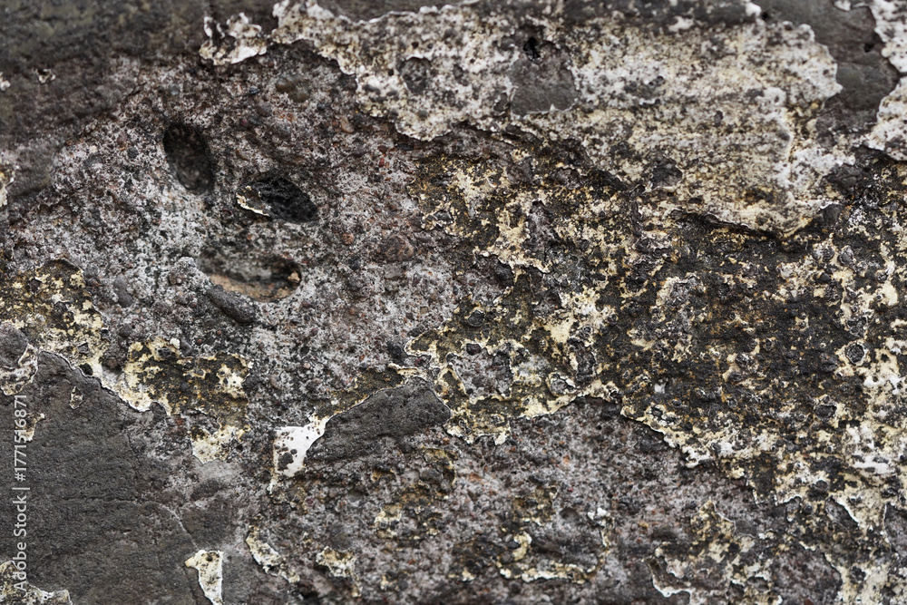 Naklejka premium Abstract macro texture of dark, weathered rock. A grunge background showing erosion, cracks, and peeling mineral deposits on a stone surface.