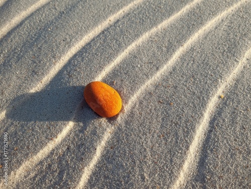 Orange Stone Casting Long Shadow on Rippled Sand, Desert-like Environment with Abstract Patterns and Natural Light, Minimalist Composition and Warm Tones