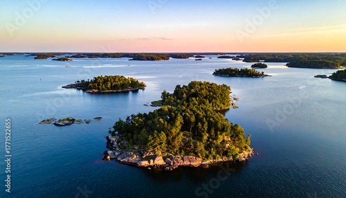 Aerial view of green tree-covered islands dotting blue waters under a warm sunset sky with soft, orange and pink hues