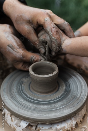 A master guides children's hands as they sculpt on a pottery wheel. Creativity, learning, and experiencing craft through experience.