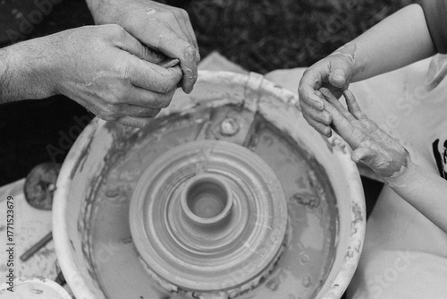 Pottery training: adult hands guide children's hands as they create a clay object on a pottery wheel. Creativity, intergenerational connection, and art all in one frame.