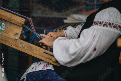 Hand weaving in traditional dress—women's hands create a colorful pattern on a wooden loom. Folk craft and cultural heritage.