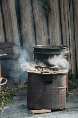 A steaming metal cauldron in the open air. The atmosphere of a rustic kitchen, traditional cooking over a fire.
