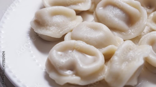 revolves. Boiled dumplings and cream are arranged in a circle on a white plate. The plate with dumplings is set against a light background, creating a simple and appetizing composition.