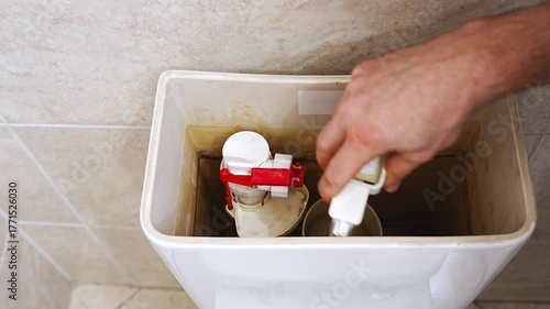 Men's hands are disassembling the toilet tank. repair of plumbing in the toilet or bathroom.