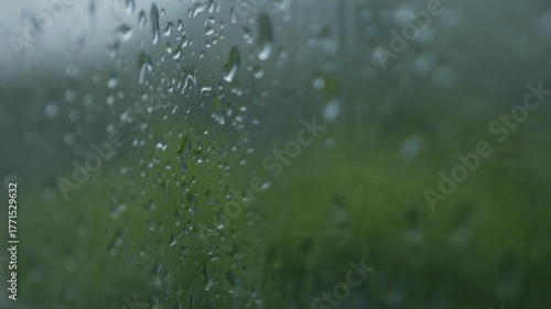 Closeup of raindrops slowly sliding down glass window with blurred city background creating calm reflective mood. Rainy window.