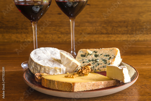 Plate with various french cheeses and glasses of red wine on a wooden table; close up